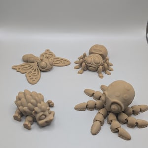 Könnte beinhalten: Eine Sammlung von vier hellbraunen, beweglichen Figuren mit matter Oberfläche. Das Set besteht aus einem Schmetterling mit gemusterten Flügeln, einer Spinne mit großen Augen, einem stacheligen igelartigen Wesen und einem Oktopus mit segmentierten Tentakeln.
