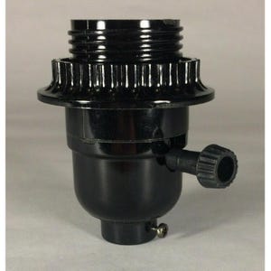 May include: A black lamp socket featuring a threaded top section, a fluted collar, and a side-mounted rotary knob for operation. The cylindrical base includes a small metal screw near the bottom, providing a functional component for lighting fixtures.
