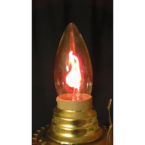 May include: A flame-tip light bulb with a clear glass exterior and an internal orange and yellow flame-shaped filament. The bulb is set into a metallic gold-colored base with a smooth, tiered design, contrasting against a dark background.