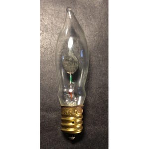 May include: A clear, flame-shaped light bulb with a pointed tip and a metallic base. Inside the glass, a small, flat, circular dark element is visible, connected to a thin stem with a green accent. The brass-colored screw base is marked 130V7W/CHINA.