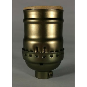 May include: A metallic bronze-coloured lamp socket featuring a cylindrical body with a smooth finish, a lower section with a series of small rectangular cutouts, and a circular top cap made of a light brown cork-like material with a screw base.
