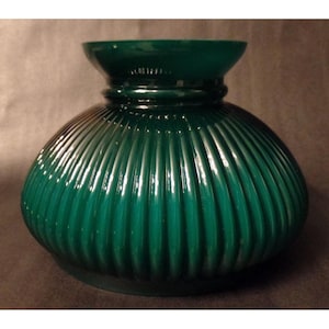 May include: A dark emerald green glass lamp shade featuring a rounded, bulbous body with vertical ribbed detailing and a wide, flared opening at the top. The glass has a smooth, glossy finish that reflects light along the curved, fluted surface.