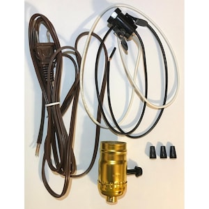 May include: A collection of lamp parts, including a brown power cord, black and white wires, a gold-colored lamp socket, and three black wire connectors. The components are arranged against a white background, suggesting a DIY or repair theme.