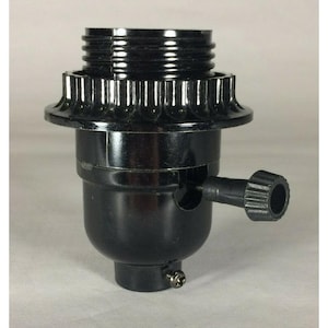 May include: A black lamp socket featuring a threaded top section for bulb installation, a decorative fluted collar, and a side-mounted rotary turn knob switch. The base includes a small metal set screw for secure attachment to a lamp pipe or fixture.