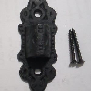May include: A black, ornate metal wall sconce with two matching screws. The sconce has a decorative, scrolled design and a cylindrical holder. The screws are dark brown and have a pointed tip.