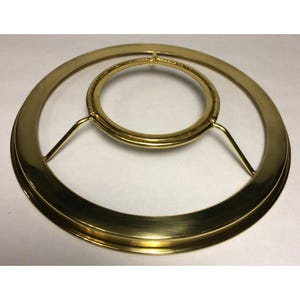 May include: A gold-colored lamp shade ring with a circular design. The ring has a large outer circle and a smaller inner circle, connected by three support bars. The metal has a shiny, reflective surface.