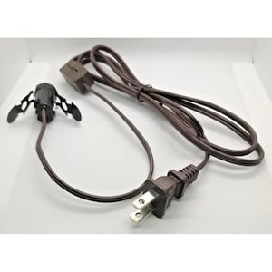 Op de afbeelding: Een bruin elektrisch snoer met een tweepolige stekker, een ingebouwde tuimelschakelaar en een kleine zwarte fitting met twee metalen veerclips aan de zijkanten voor een veilige bevestiging in een lamp of een ander armatuur.