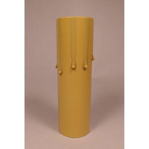 May include: A cylindrical candle cover in a matte mustard yellow finish. The exterior features raised, vertical drip-like textures extending from the top rim downward, mimicking the appearance of melted wax on a traditional pillar candle.