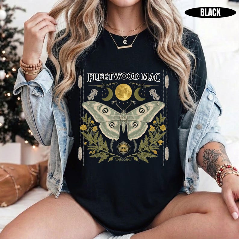 Może przedstawiać: Czarny t-shirt z nadrukiem graficznym przedstawiającym dużą ćmę umieszczoną centralnie nad ż&oacute;łtymi kwiatami i paprociami. Nad ćmą znajduje się ż&oacute;łty księżyc oraz napis "FLEETWOOD MAC" białymi wielkimi literami. Wz&oacute;r zawiera ozdobne linie.
