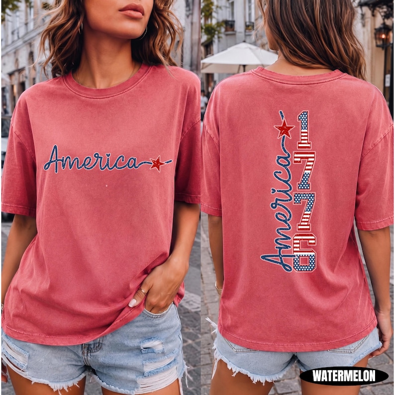 May include: A watermelon-colored short-sleeve t-shirt featuring a front graphic with the word America in blue script and a red star. The back graphic displays the word America vertically next to the number 1776 in red, white, and blue flag patterns.
