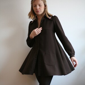 May include: A brown, long-sleeved dress with a flared skirt and a button-up front. The dress has a small pocket on the left side and a floral embroidery detail on the collar.