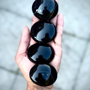 Könnte beinhalten: Vier glatte, polierte, runde schwarze Steine sind vertikal gestapelt. Jeder Stein hat eine glänzende, reflektierende Oberfläche mit feinen, hellen natürlichen Einschlüssen oder Adern, die sich über das dunkle Material ziehen.