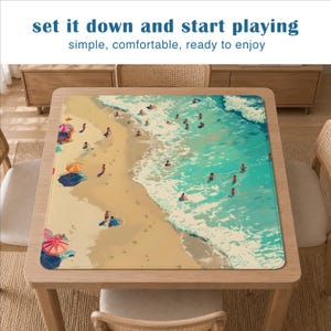 Peut inclure: Un tapis de table rectangulaire repr&eacute;sentant une sc&egrave;ne de plage vue du dessus avec du sable beige, une eau turquoise et de petites silhouettes de personnes nageant et se relaxant sous des parasols color&eacute;s. Le texte "set it down and start playing" et "simple, comfortable, ready to enjoy" est imprim&eacute; au-dessus du tapis.