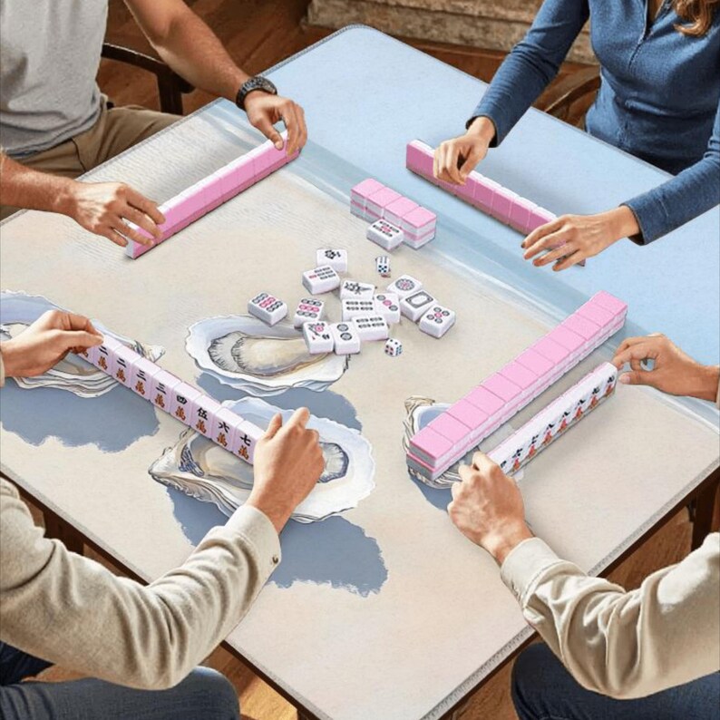 May include: A square mahjong table mat featuring a light beige surface with blue and white oyster shell illustrations. Four sets of pink mahjong tile racks are positioned at the edges, with scattered white mahjong tiles in the center of the mat.