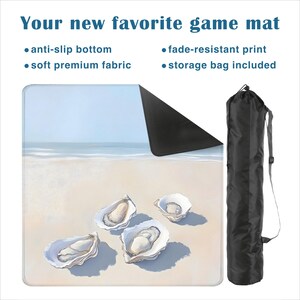 May include: A square game mat featuring a beach scene with four oyster shells on the sand, an anti-slip black bottom, and a soft fabric top. The text reads: Your new favorite game mat, anti-slip bottom, fade-resistant print, soft premium fabric, storage bag included. A black storage bag is shown to the right.