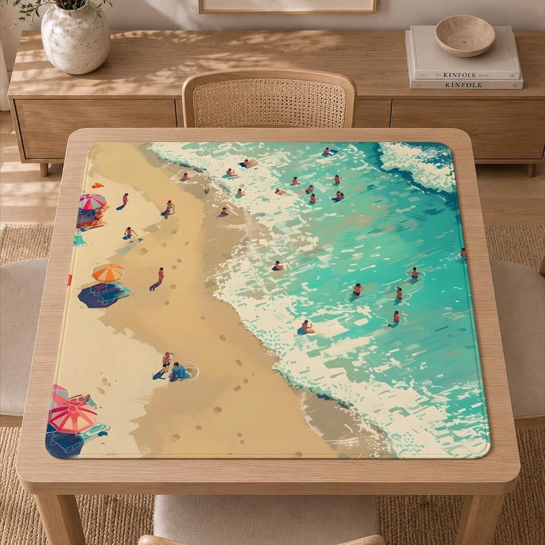 Peut inclure: Un tapis de bureau carr&eacute; pr&eacute;sentant une illustration a&eacute;rienne d'une plage de sable rencontrant une eau turquoise. La sc&egrave;ne comprend des parasols color&eacute;s, de petites silhouettes de personnes nageant dans les vagues et se relaxant sur le sable.