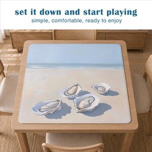 May include: A square game mat featuring a beach scene with four open oyster shells on the sand. The text "set it down and start playing" and "simple, comfortable, ready to enjoy" is printed in blue and gray at the top of the image.