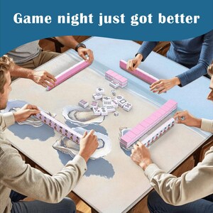 May include: A square mahjong table mat featuring a light beige surface with blue oyster shell illustrations. Four players are positioned around the mat, each with a pink tile rack. The center contains scattered white mahjong tiles. Text reads: Game night just got better.