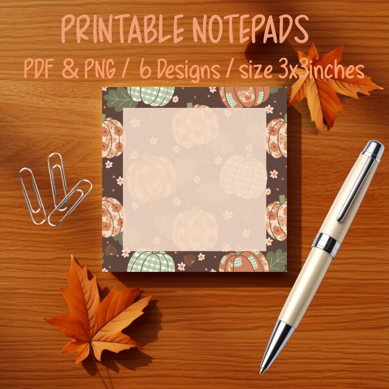 May include: A square notepad featuring a dark brown border with a repeating pattern of pumpkins and small flowers. The centre is a light beige square for writing. The notepad is 7.62x7.62 cm and is accompanied by three silver paper clips and a pen.