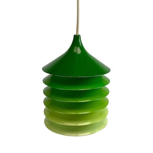 Könnte beinhalten: Grüne Pendelleuchte mit geschichtetem, konischem Design. Die Leuchte weist einen Farbverlauf von Grüntönen auf, der von einem tiefen Grün oben zu einem helleren, gelblich-grünen Farbton unten übergeht. Die Leuchte hängt an einem dünnen, cremefarbenen Kabel.