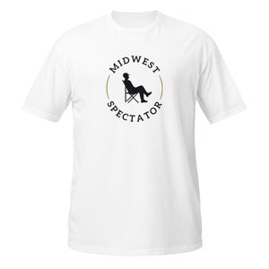 Puede incluir: Camiseta blanca con un gráfico circular. El gráfico presenta las palabras "Midwest Spectator" alrededor de una silueta de una persona relajándose en una silla. La persona lleva un sombrero.