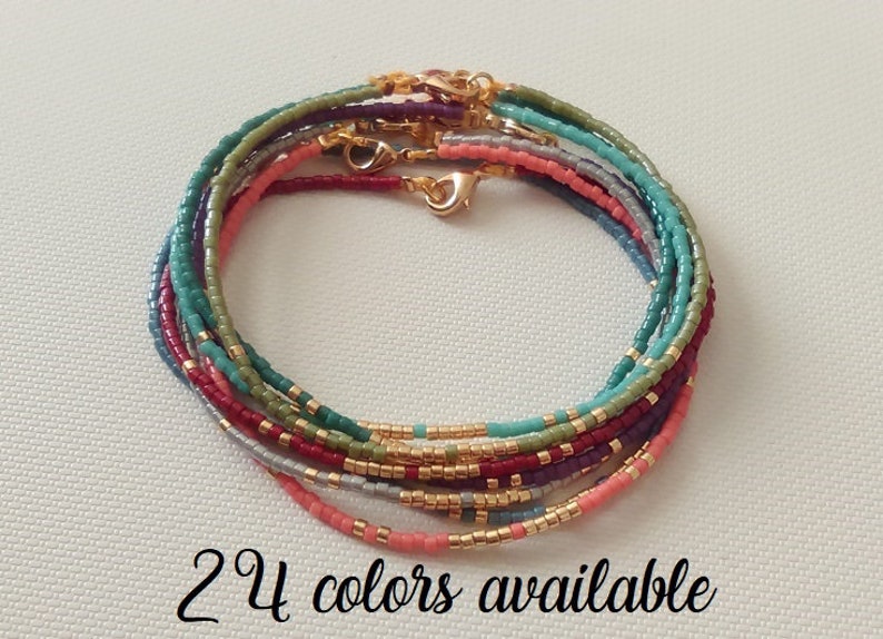 Puede incluir: Un conjunto de pulseras de cuentas en varios colores, incluyendo turquesa, rosa, morado y verde. Cada pulsera presenta cierres y detalles dorados. El texto "24 colores disponibles" est&aacute; escrito en cursiva en la parte inferior de la imagen.
