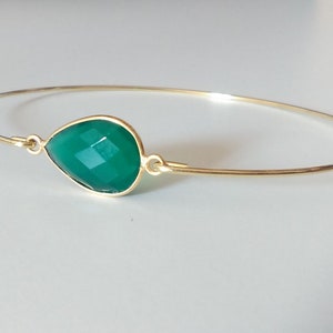 May include: A gold bangle bracelet with a teardrop-shaped green gemstone.