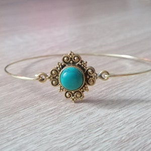 May include: A gold bangle bracelet with a turquoise gemstone set in a decorative, ornate design.