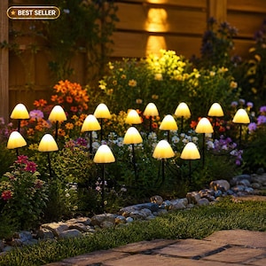May include: Illuminated mushroom garden lights with yellow glowing caps and black stems. The lights are arranged among colorful flowers and greenery, creating a whimsical outdoor ambiance. The image includes a "Best Seller" badge.