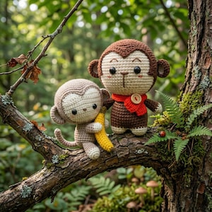 Könnte beinhalten: Zwei gehäkelte Affenpuppen auf einem Ast. Einer hält eine gelbe Banane, der andere trägt einen roten Schal mit einem Holzknopf. Die Affen sind braun, beige und weiß.