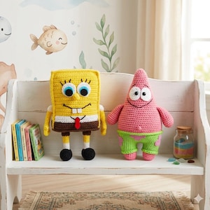 May include: Two crocheted character dolls, SpongeBob SquarePants and Patrick Star, sit on a white bench. SpongeBob is yellow with a brown bottom, and Patrick is pink with green shorts. The background features a wall mural with fish and seaweed.