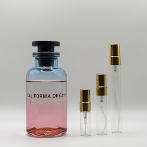 May include: A perfume bottle with a black cap and a blue and pink gradient, labeled "CALIFORNIA DREAM LOUIS VUITTON." Three smaller, clear spray bottles with gold caps are next to it. The bottles are on a white background.
