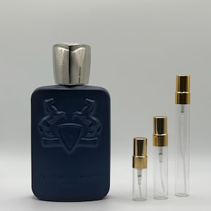 May include: A navy blue perfume bottle with a silver cap and three clear glass vials with gold-colored spray tops. The perfume bottle has a crest design and the words "Parfums de Marly" printed on the front.