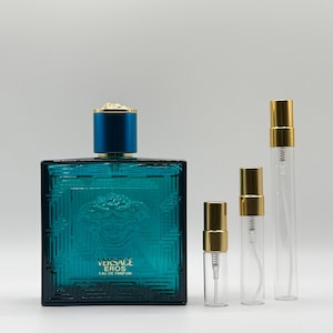 May include: A teal-colored rectangular perfume bottle with a gold cap and the text "VERSACE EROS EAU DE PARFUM". Several clear glass spray bottles with gold caps are also present. The perfume bottle has a textured design.