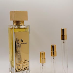 May include: A rectangular glass perfume bottle with a gold cap and a gold label featuring the text Swiss Arabian Essence of Casablanca Extrait de Parfum, accompanied by three smaller clear glass sample vials with gold spray pump caps.