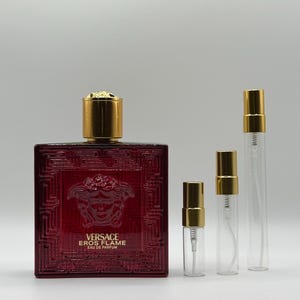 May include: A red Versace Eros Flame Eau de Parfum bottle with a gold cap, alongside three clear atomizer bottles with gold caps. The perfume bottle has a textured design and the Versace logo.