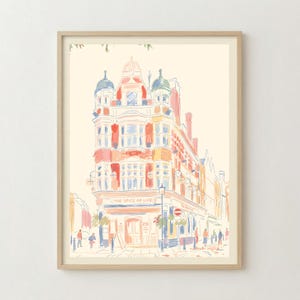 May include: A framed art print featuring a watercolour-style illustration of a multi-storey building with the text THE SPICE OF LIFE visible on the facade. The architectural drawing uses soft tones of red, blue, and yellow on a cream background.