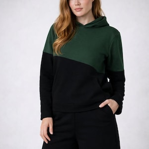 Könnte beinhalten: Ein langärmeliger Kapuzenpullover mit einem Color-Block-Design, bestehend aus einem dunkelgrünen Oberteil und einem schwarzen Unterteil, kombiniert mit passenden schwarzen Shorts. Der Hoodie verfügt über eine Kängurutasche und eine Kapuze.