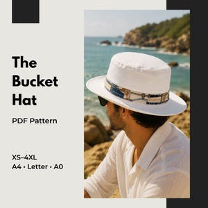 Könnte beinhalten: Ein weißer Fischerhut mit einem gemusterten Band mit blauen und goldenen geometrischen Details. Der Text links lautet: The Bucket Hat, PDF Pattern, XS-4XL, A4, Letter, A0. Der Hut wird im Freien an einer felsigen Küste am Meer getragen.
