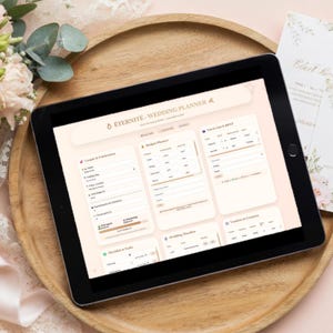 Può includere: Un tablet nero che mostra un'interfaccia di pianificazione del matrimonio, con sezioni per coppie, budget, liste degli invitati e tempistiche. Il tablet è su un vassoio di legno, con decorazioni floreali e un biglietto d'invito di nozze.