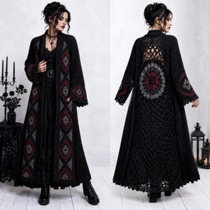 May include: A long, black, open-front crochet cardigan featuring a repeating diamond pattern in dark red and grey along the front panels. The back displays an intricate, large circular mandala-style crochet motif with a net-like openwork design.