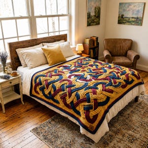 Op de afbeelding: Een gehaakte deken met een ingewikkeld, herhalend Keltisch knooppatroon in tinten mosterdgeel, diep marineblauw en bordeauxrood, met witte accenten, gedrapeerd over een bed met wit beddengoed en verschillende kussens.