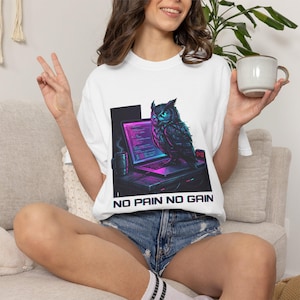 May include: White t-shirt featuring a digital art design of an owl perched on a laptop. The owl has blue eyes and is surrounded by a neon glow. The text "NO PAIN NO GAIN" is printed below the laptop.