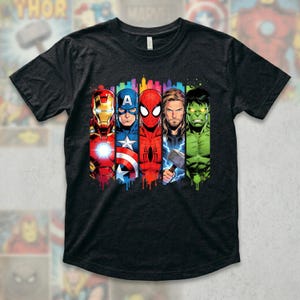 Op de afbeelding: Donkergrijs t-shirt met een kleurrijke afbeelding van Iron Man, Captain America, Spider-Man, Thor en de Hulk. De superheldenafbeeldingen zijn verticaal uitgelijnd met een stadsgezicht achtergrond en een druipend verfeffect.
