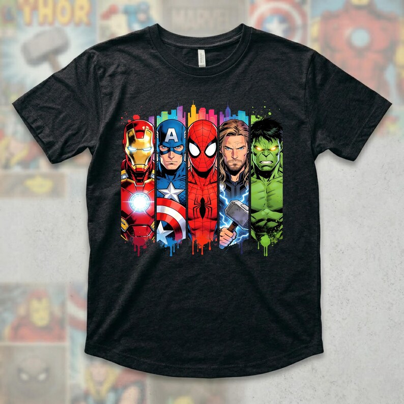 Op de afbeelding: Donkergrijs t-shirt met een kleurrijke afbeelding van Iron Man, Captain America, Spider-Man, Thor en de Hulk. De superheldenafbeeldingen zijn verticaal uitgelijnd met een stadsgezicht achtergrond en een druipend verfeffect.