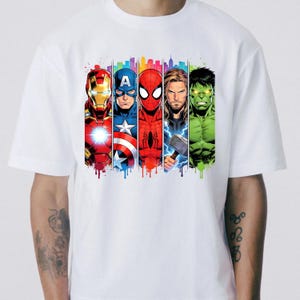 Op de afbeelding: Wit T-shirt met een kleurrijke afbeelding van vijf Marvel-superhelden: Iron Man, Captain America, Spider-Man, Thor en Hulk. Elk personage wordt afgebeeld in een verticaal paneel met een stadsgezicht op de achtergrond en een verfeffect.