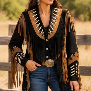 May include: Black suede jacket with brown fringe and accents. The jacket features a decorative collar and sleeve details with silver studs and bone-like beads. A silver buckle belt and a black cowboy hat complete the western look.