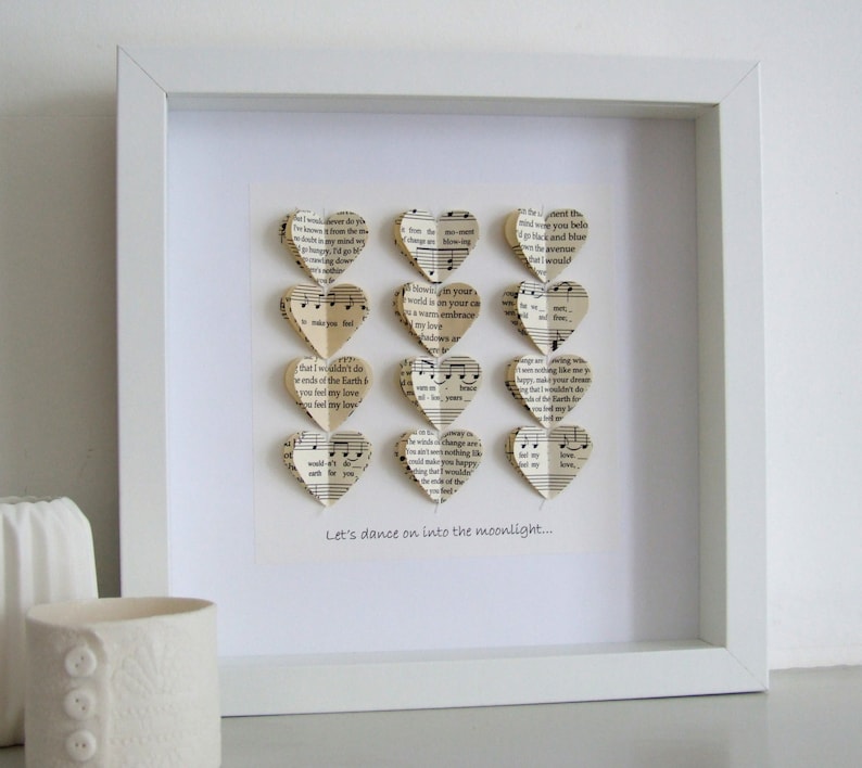 May include: A white frame with a white mat and a white background. The frame contains a collection of paper hearts made from sheet music. The hearts are arranged in a vertical row. The text "Let's dance on into the moonlight..." is printed below the hearts.