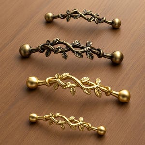 Può includere: Quattro maniglie per armadietti in metallo disposte in fila, caratterizzate da un design a vite intrecciata con piccole foglie. Due maniglie hanno una finitura bronzo scuro e due hanno una finitura oro brillante. Ogni maniglia termina con una sfera.