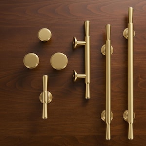 May include: A collection of brushed gold hardware including three circular knobs, one T-shaped handle, and two long cylindrical bar pulls. Each piece features a smooth, matte metallic finish with clean lines and a uniform, solid gold-toned appearance.